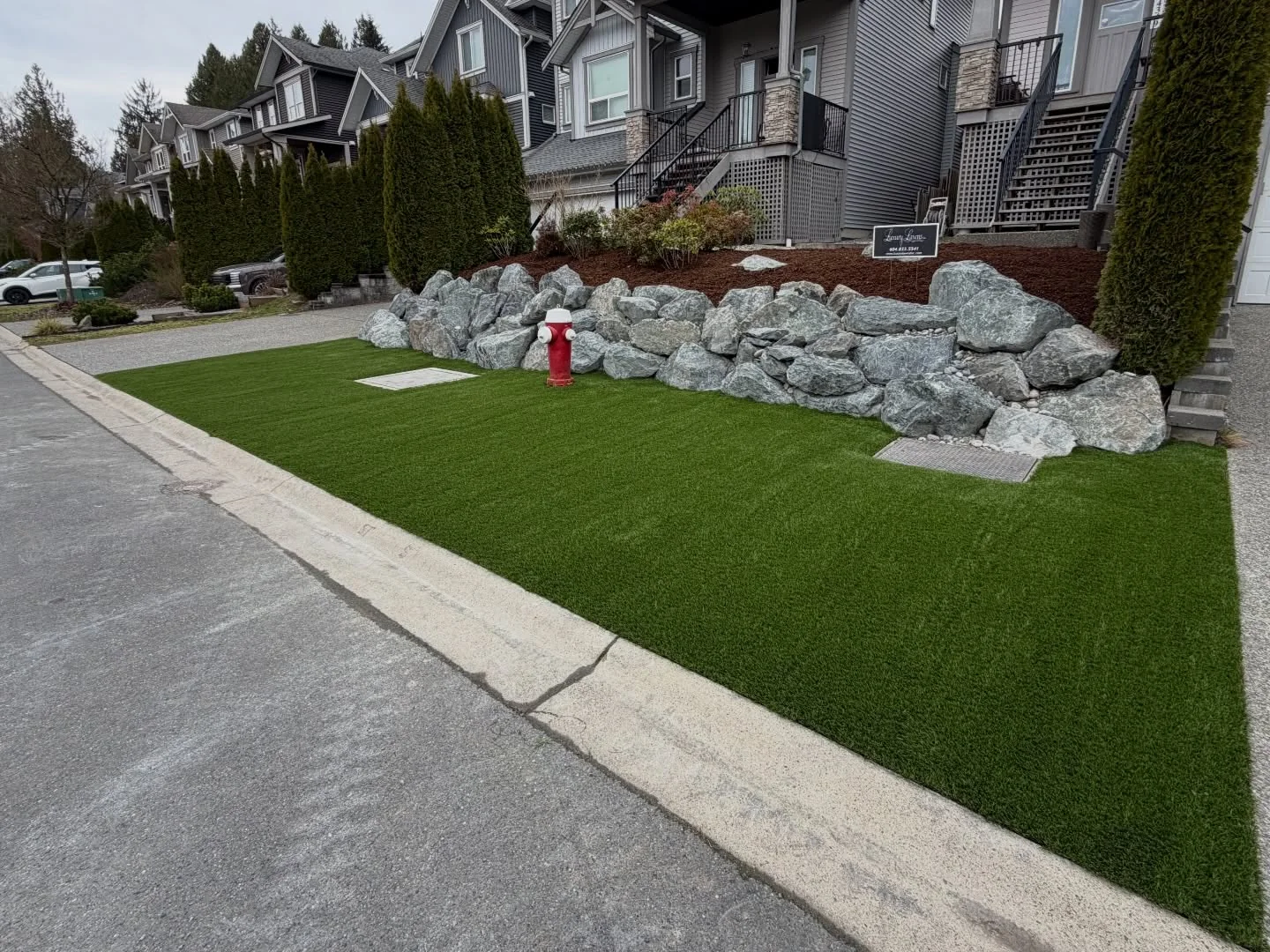 Luxury Lawns front-yard turf installation alongside a stone retaining wall and paving